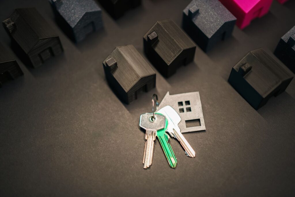 Llaves de una casa junto a maquetas de viviendas, representando la decisión entre alquilar o comprar